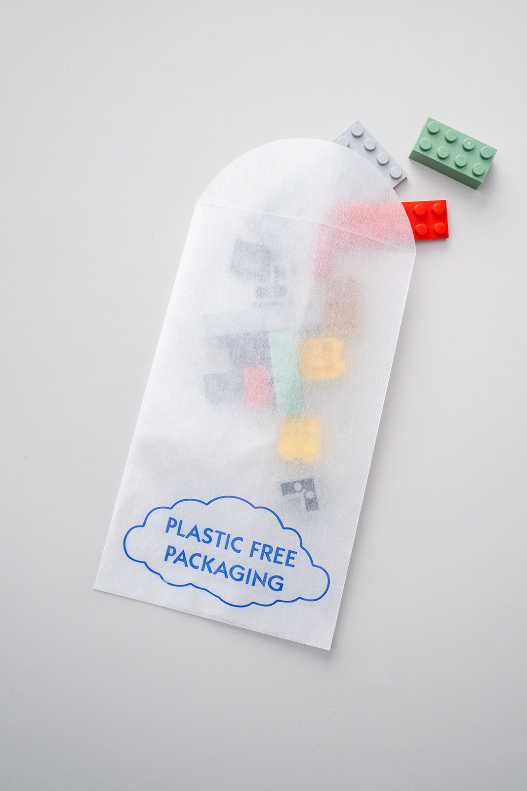 Building brick toys are visible inside of a translucent paper envelope made of glassine and marked with "Plastic Free Packaging" on the side.