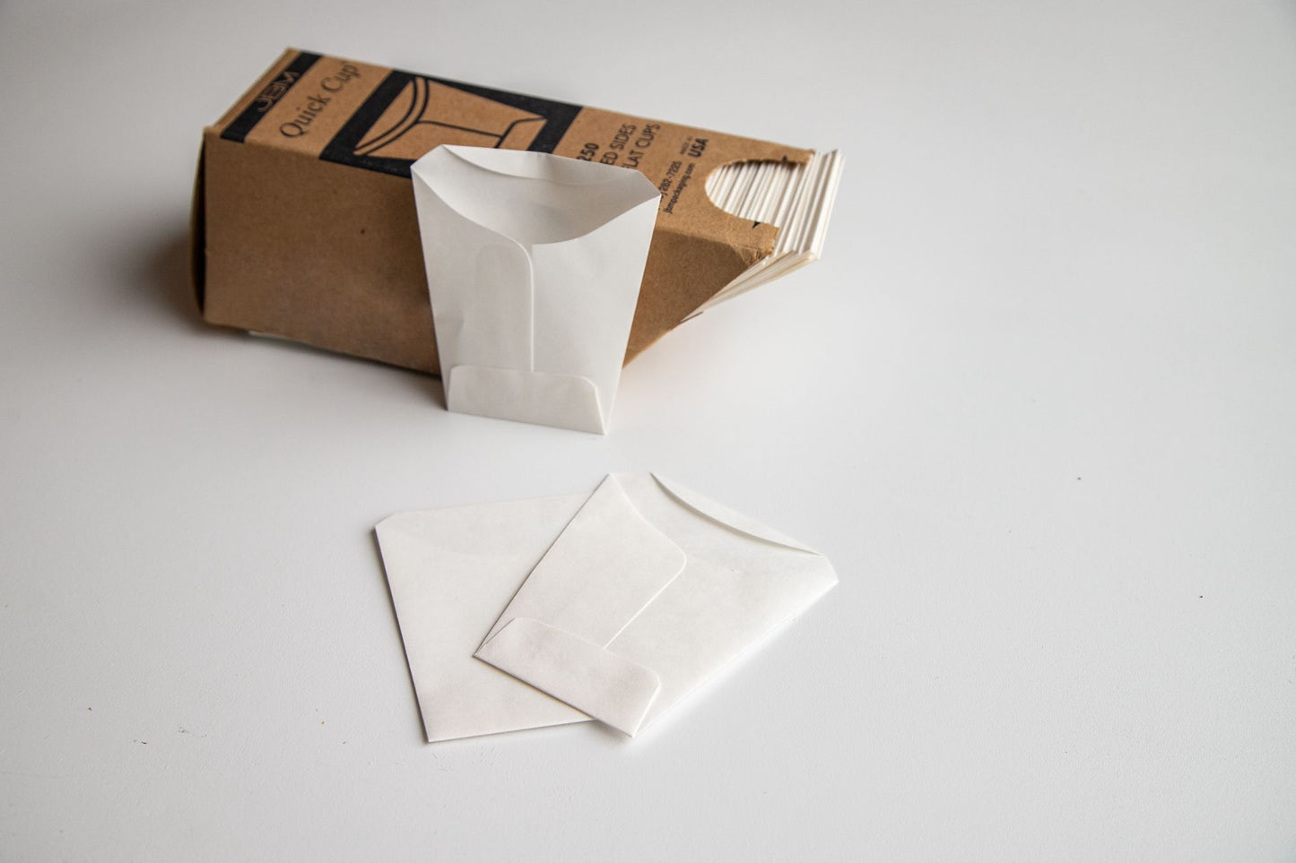 Brown quick cup box filled with disposable cups, with three white cups displayed next to it. 